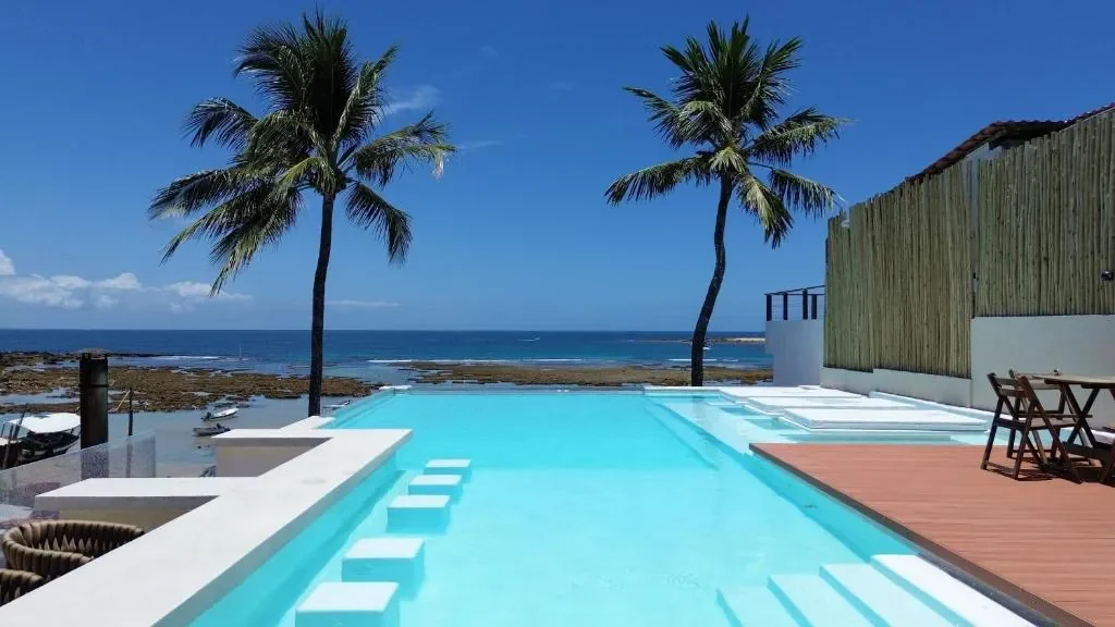 Piscina da Chez Max com coqueiros e mar ao fundo.